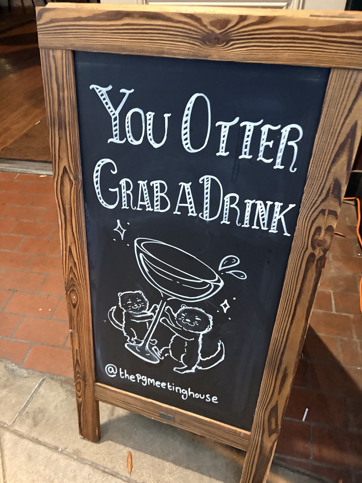 Chalkboard sign outside the PG Meetinghouse reading You Otter Grab a Drink